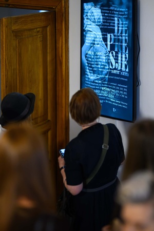 Wystawa: Depresje - Publiczność czytająca tekst opisowy do wystawy.