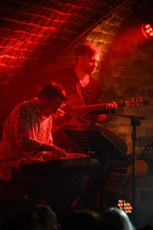 Koncert - Pracownia Piosenki "O jesieni..." - Grzegorz Gawlik przy pianinie i Arek Boryczka przy gitarze w czerwonym świetle.